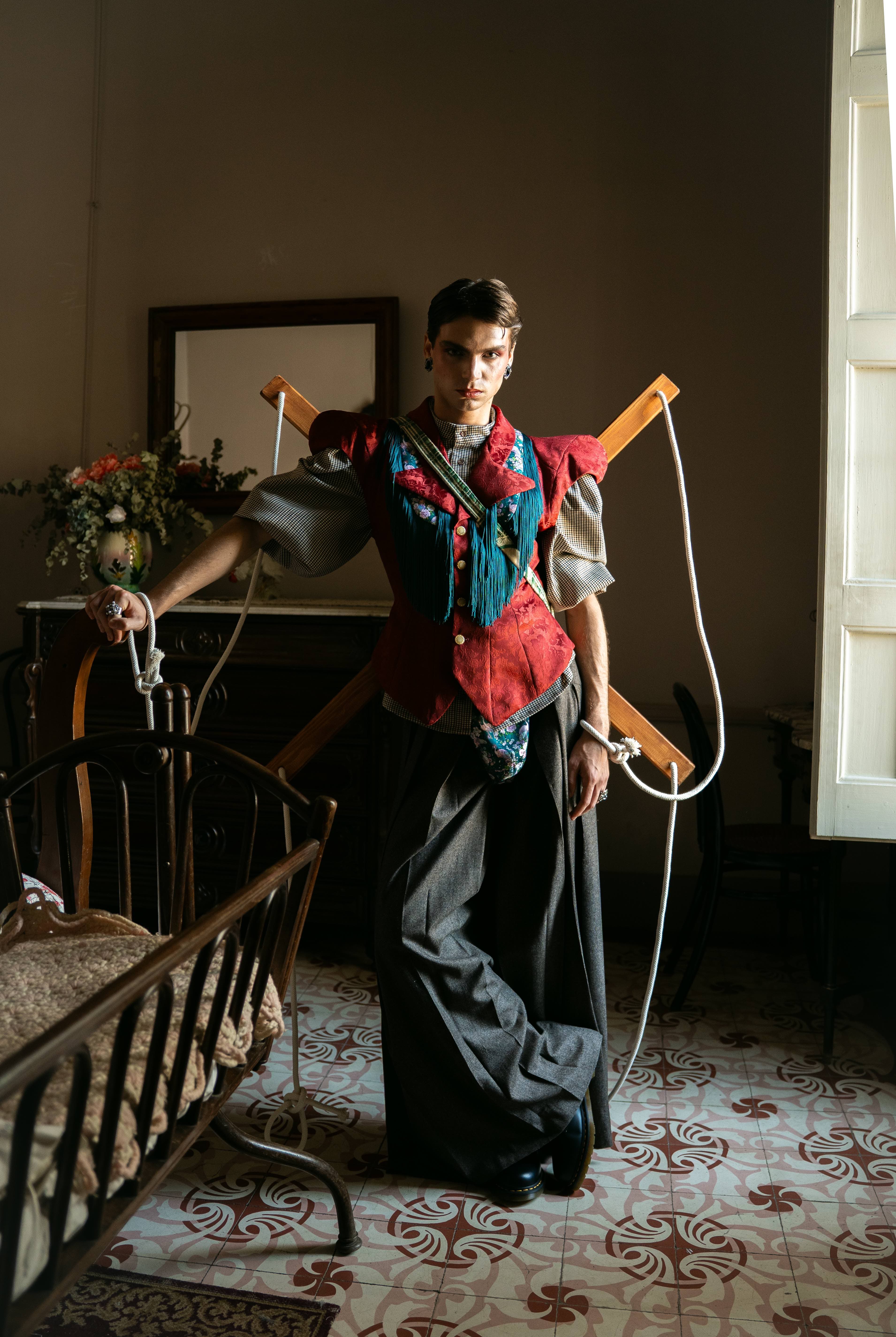 Mona Puppet Riot FW25 — model with puppet strings and colorful layered vest, theatrical fashion Barcelona